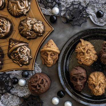 Six golden-brown monster mask cakelets with scary faces baked in Nordic Ware aluminum cakelet pan