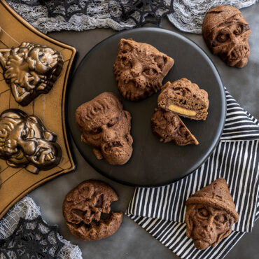 Six golden-brown monster mask cakelets with carved pumpkin faces baked in Nordic Ware aluminum pan