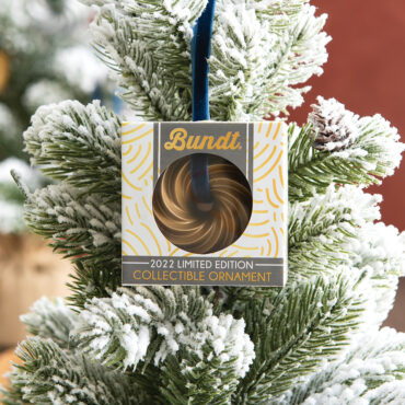 Nordic Ware gold Heritage Bundt ornament hanging on Christmas tree branch with festive lighting