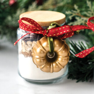 Two miniature gold-finished bundt pan ornaments displayed in glass jars as holiday decorations