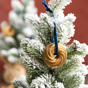 Nordic Ware gold-colored Heritage bundt pan ornament hanging on green Christmas tree branch