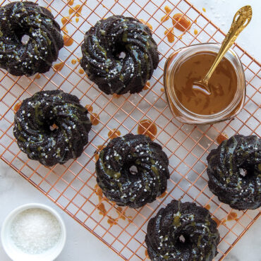 Six chocolate bundt cakes with caramel glaze on copper cooling rack, baked in Nordic Ware Swirl Bundtlette pan