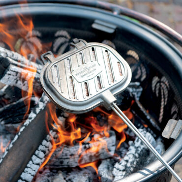 Nordic Ware cast aluminum campfire griller closed over open flames with glowing orange embers
