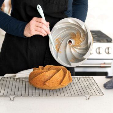 Person using Nordic Ware bundt extraction tool with curved edge to remove cake from fluted bundt pan