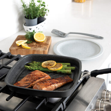 Nordic Ware Verde ceramic nonstick searing grill pan on stovetop cooking salmon fillet with grilled vegetables