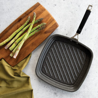 Nordic Ware Verde ceramic nonstick searing grill pan with ridged surface, surrounded by fresh chopped vegetables