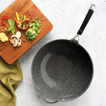 Nordic Ware Verde ceramic nonstick wok with dark green interior, surrounded by fresh stir fry ingredients