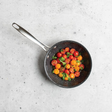 Nordic Ware Basalt 8-inch nonstick sauté skillet with cherry tomatoes, dark charcoal finish on concrete surface