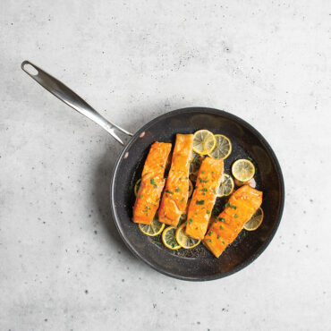 Nordic Ware Basalt 12-inch nonstick skillet with seared salmon fillet, dark gray finish on concrete surface