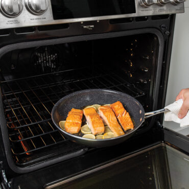 Nordic Ware Basalt 12-inch skillet with salmon fillet being placed in oven, dark non-stick surface
