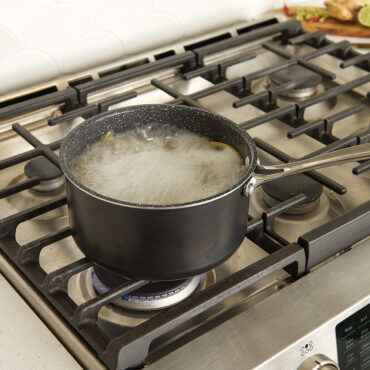 Nordic Ware Basalt dark gray 3-quart sauce pan on stovetop with boiling pasta water