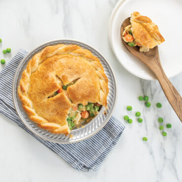 Golden chicken pot pie with flaky crust in Nordic Ware aluminum mini pie pan with serving spoon