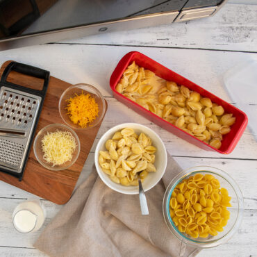 Nordic Ware white plastic microwave pasta cooker with prepared creamy mac and cheese, rectangular container with lid