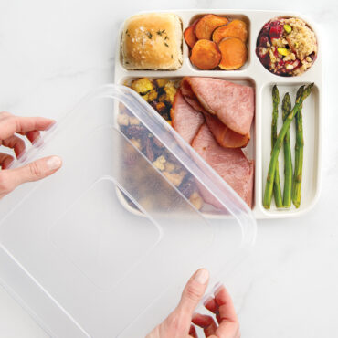 Hand placing clear lid on Nordic Ware divided dinner tray containing leftover food portions