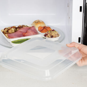 Gray Nordic Ware divided dinner tray with lid being reheated in microwave, containing cooked food portions