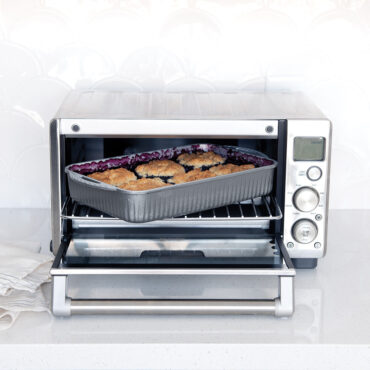 Golden berry cobbler in Nordic Ware ProCast aluminum baking pan being removed from toaster oven with oven mitt
