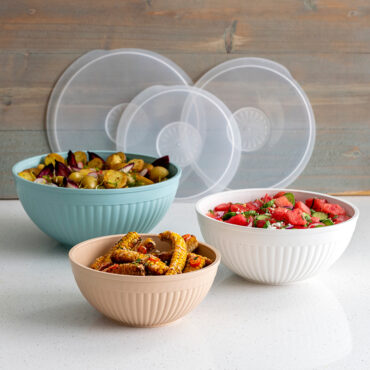Three white ceramic bowls with matching lids containing colorful prepared foods, part of Nordic Ware 6-piece covered bowl set