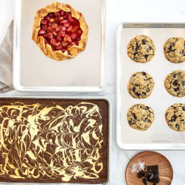 Three Nordic Ware aluminum half sheet pans with baked desserts: berry galette, golden chocolate chip cookies, and fudgy brownies