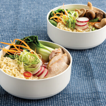 Two white ceramic Nordic Ware soup bowls filled with noodle soup containing vegetables and broth
