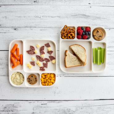 Two Nordic Ware divided meal trays with compartments containing colorful kids' meals including sandwiches, fruits, and snacks