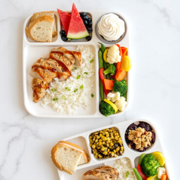 Two Nordic Ware divided meal trays filled with colorful food portions: chicken, rice, vegetables, fruit, and cupcake