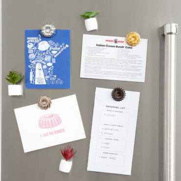 Four colorful bundt cake-shaped magnets on white refrigerator door holding handwritten notes and papers