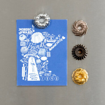 Four colorful bundt-shaped magnets holding Nordic Ware Minnesota state illustration on white refrigerator door