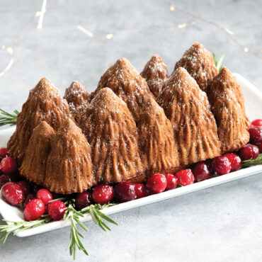 Nordic Ware aluminum loaf pan with detailed alpine forest design featuring trees and mountains, displayed on red cranberries