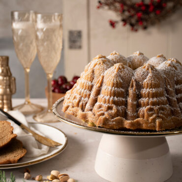 Golden bundt cake with powdered sugar from Nordic Ware Very Merry Bundt pan, champagne glass in background