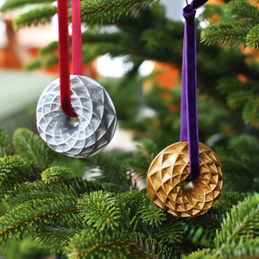 Two Nordic Ware collectible cast metal Jubilee Bundt ornaments in gold and silver finishes hanging on Christmas tree
