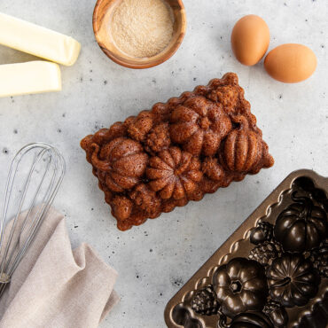 Golden pumpkin spice loaf cake sliced on cutting board with Nordic Ware aluminum Harvest Bounty pan and ingredients