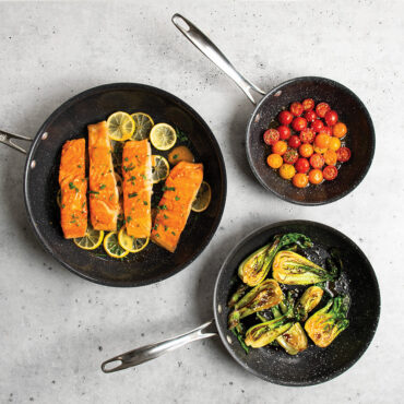 Nordic Ware Basalt 3-piece nonstick skillet set in charcoal gray with seared vegetables and meat displayed