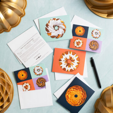 Nordic Ware bundt greeting cards displayed on blue surface with gold aluminum bundt pans and pen