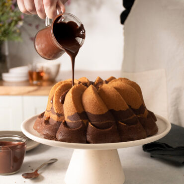 Golden bundt cake with spiraled ridged design being drizzled with white glaze from Nordic Ware Pirouette pan