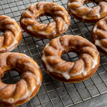Six golden-brown French twist donuts with white glaze, baked in Nordic Ware aluminum donut pan on cooling rack