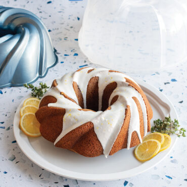 Nordic Ware aluminum swirl bundt pan with clear plastic cake keeper dome, silver finish with intricate spiral design