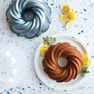Nordic Ware aluminum Swirl Bundt pan with clear plastic dome cake keeper, silver finish with decorative swirled pattern