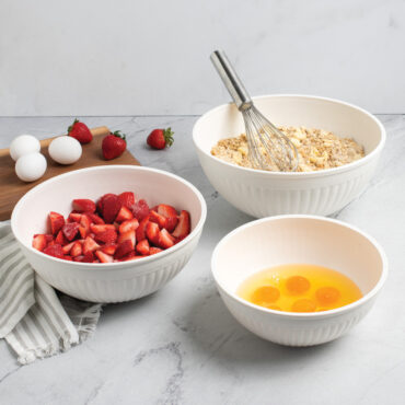 Nordic Ware 3 piece white prep and serve 5 quart, 3.5 quart and 2 quart bowls on kitchen countertop filled with strawberries, eggs and dough