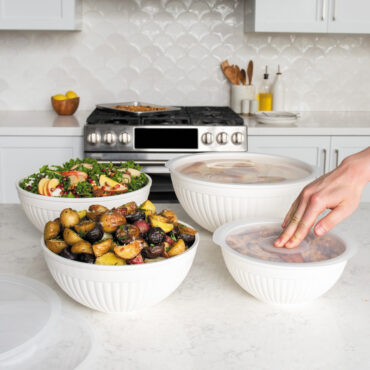 Nordic Ware 8 piece white bowl set including 7, 5, 3.5 and 2 quart bowls with lids on countertop; hand pushing lid onto a bowl