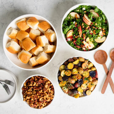 Nordic Ware 8 piece white bowl set including 7, 5, 3.5 and 2 quart bowls filled with salad, rolls, potatoes and mixed nuts