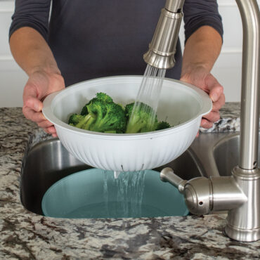 Nordic Ware sea glass green colander with matching bowl, rinsing fresh green broccoli florets under running water