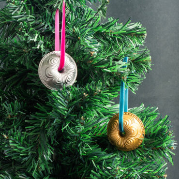 Two Nordic Ware miniature cast aluminum Chiffon Bundt ornaments in silver and gold finishes hanging on Christmas tree