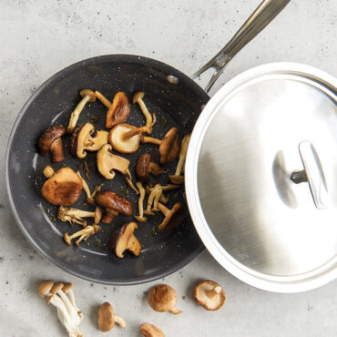 Nordic Ware 10-inch Basalt cast aluminum skillet with glass lid, containing sautéed golden mushrooms