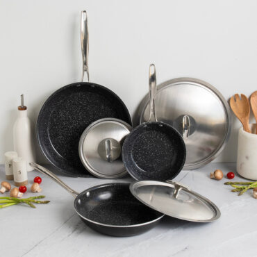 Nordic Ware Basalt non-stick sauté pan and skillet set with lids, dark gray finish, displayed with fresh ingredients