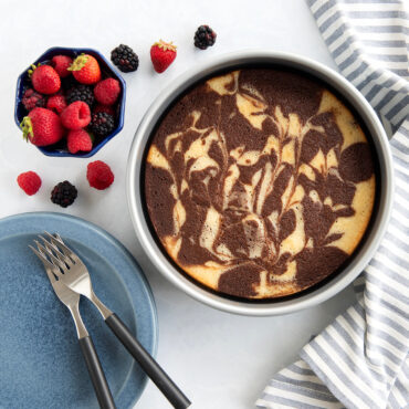 Nordic Ware aluminum round cake pan with marbled pound cake, fresh berries, and table setting overhead view