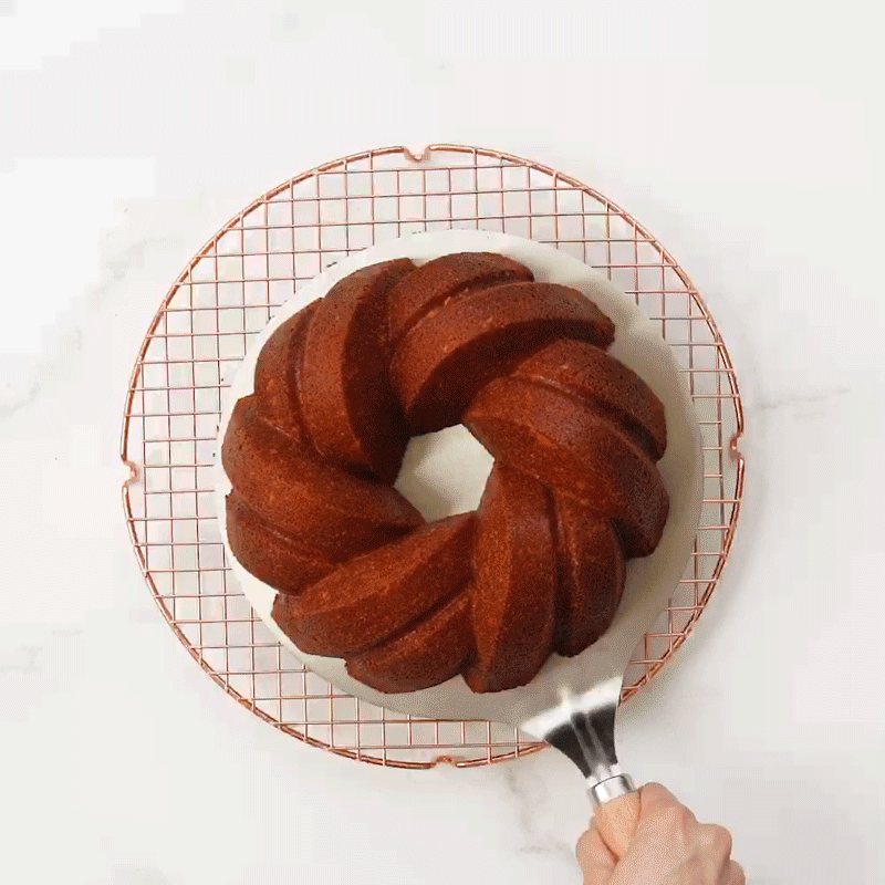 Gif of the Nordic Ware Cake Lifter picking up a 75th Anniversary Bundt Cake off of a round cooling grid and moving it to a Cake Keeper.