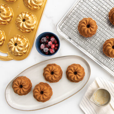 Nordic Ware aluminum Pirouette Bundtlette pan with golden spiral-shaped mini cakes on cooling rack and plate