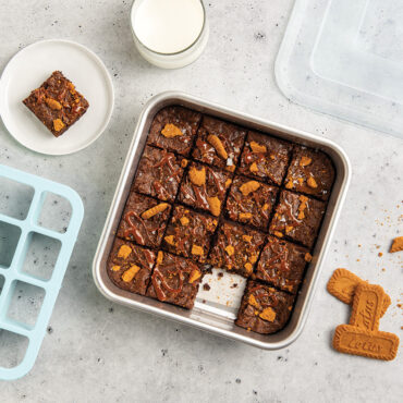 Nordic Ware brownie baking set with aluminum pan of cut brownies and metal cutting tool, one square plated