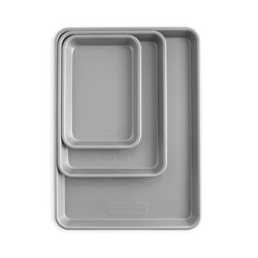 Three Nordic Ware nonstick baking sheet pans in graduated sizes, dark gray finish, arranged overhead on white background