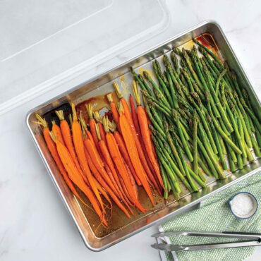 Nordic Ware aluminum roasting pan with lid, containing roasted carrots and asparagus, natural silver finish